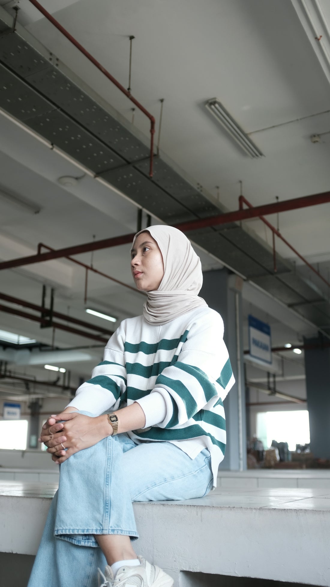A woman wearing a hijab and striped sweater sits.