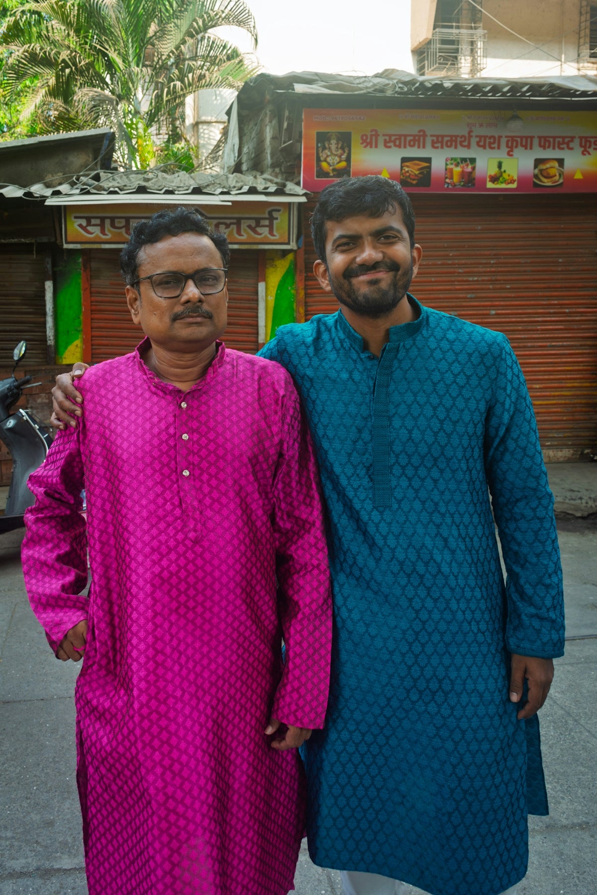 Two men in colorful kurtas stand together.